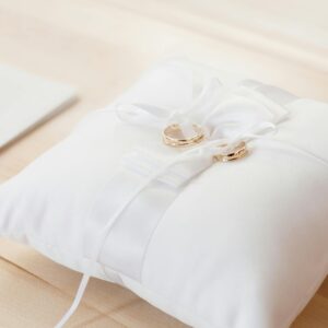 Gold wedding rings elegantly displayed on a white satin pillow, symbolizing love and commitment.